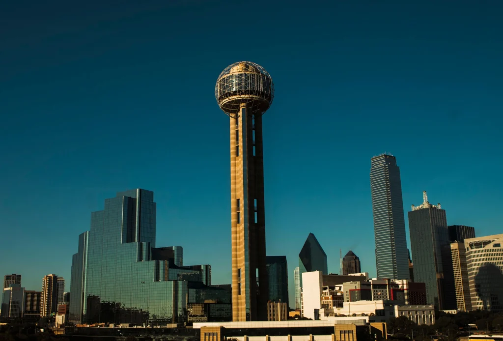 Downtown Dallas skyline with the Reunion Tower spherical observation deck rising above glass skyscrapers against a clear blue sky.