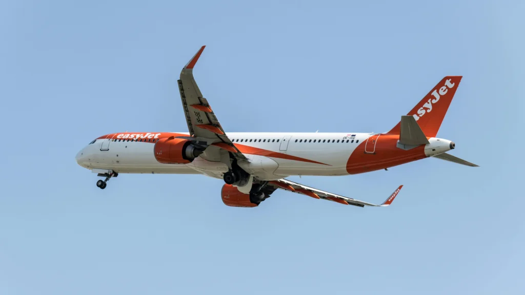EasyJet passenger jet in mid-flight with gear down against a clear blue sky.