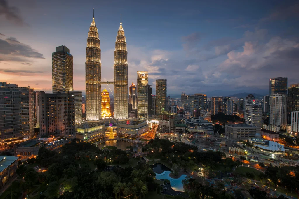 Evening cityscape of Kuala Lumpur with the illuminated Petronas Twin Towers and surrounding skyscrapers in silhouette and glow.