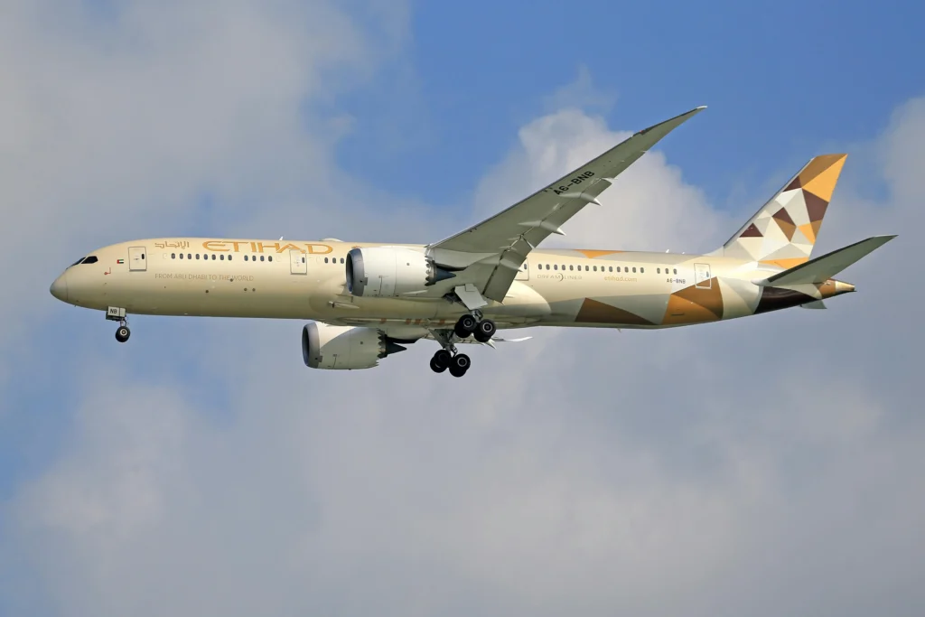 Etihad Airways Dreamliner in flight with landing gear extended against a blue sky.