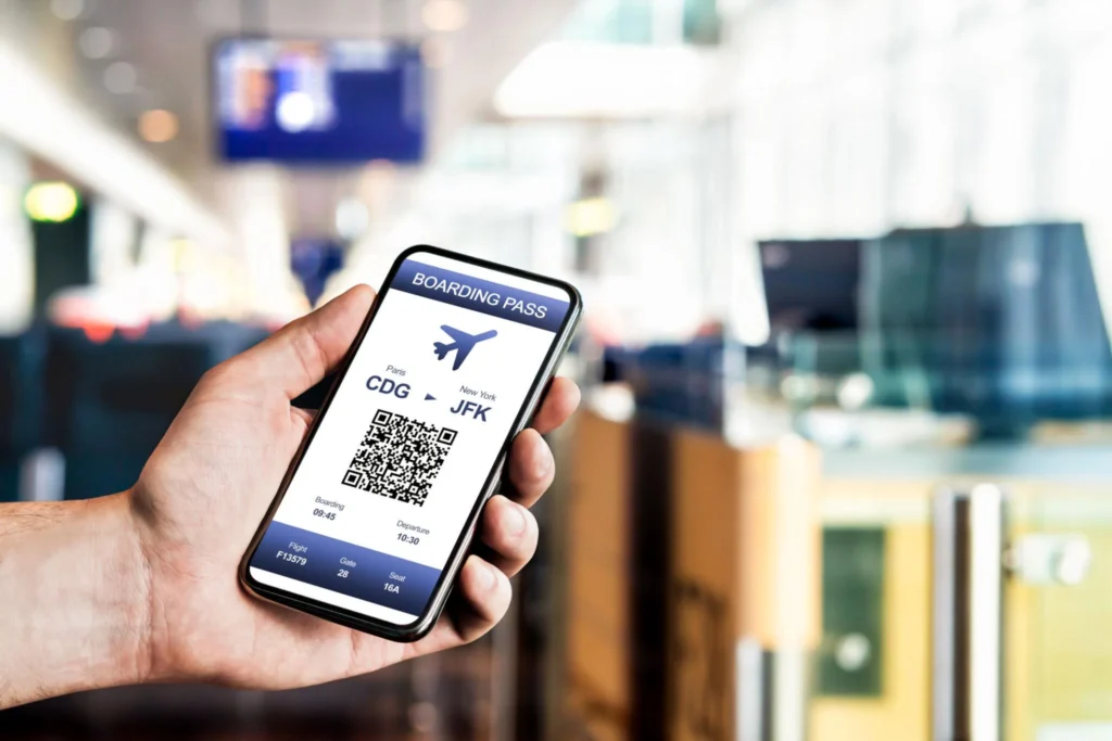 Person holding a smartphone at an airport showing a digital boarding pass with a QR code on the screen