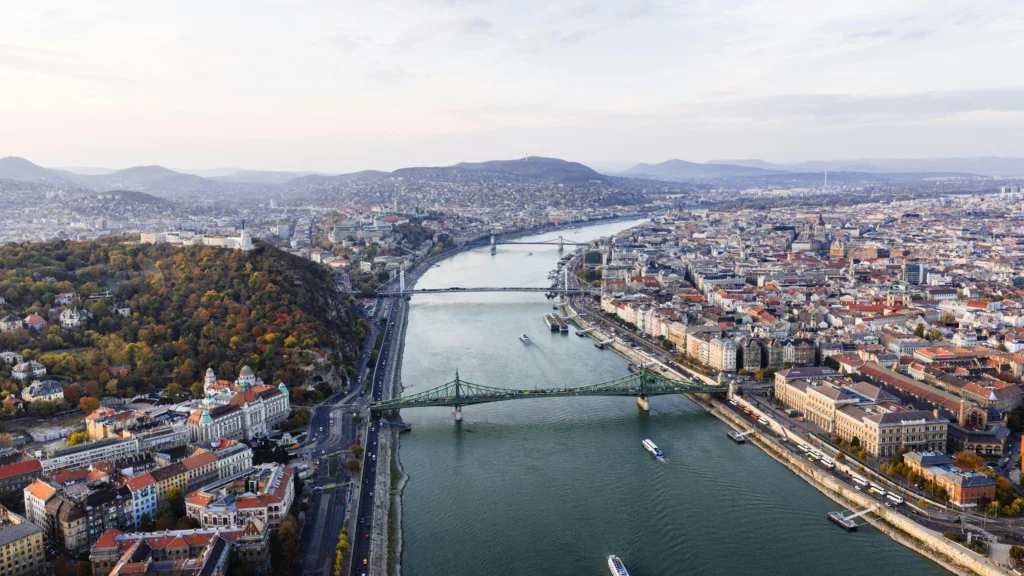 Aerial view of a river running through a European city with multiple bridges and distant hills on the horizon, daytime light. (informative)