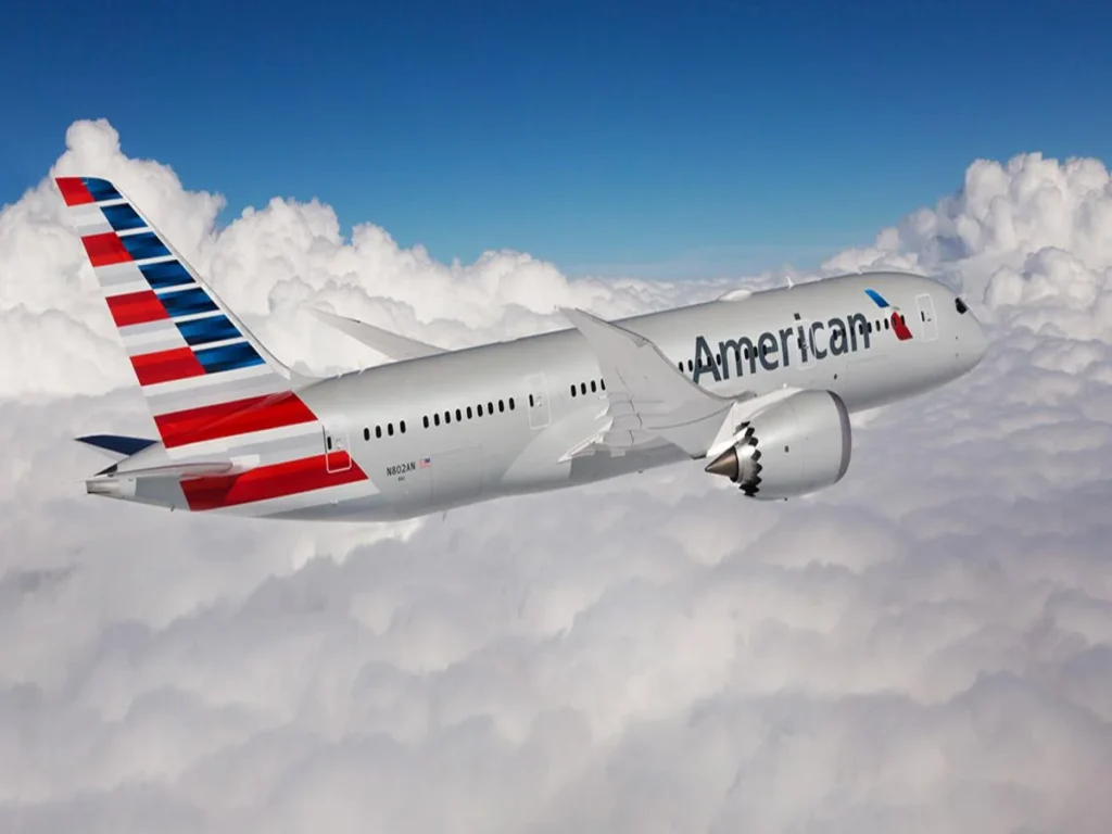 American Airlines jet soaring above fluffy clouds with a blue sky backdrop.