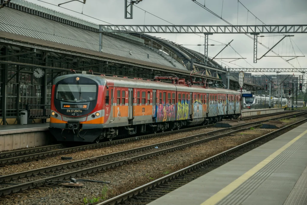 Red electric passenger train at a city station platform with graffiti along the car sides and overhead power lines above.