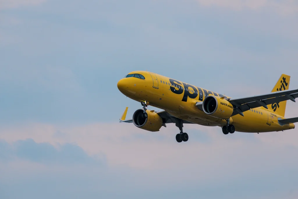 Yellow Spirit Airlines jet in flight with landing gear down against a blue sky backdrop.