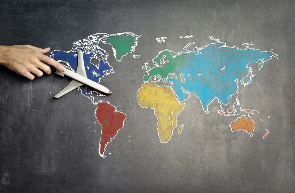 Hand holding a small model airplane over a chalk-drawn world map on a dark chalkboard, suggesting global travel.
