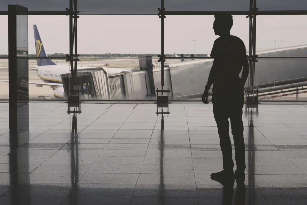 Silhouette of a man standing inside an airport terminal, looking toward aircraft outside through large glass walls
