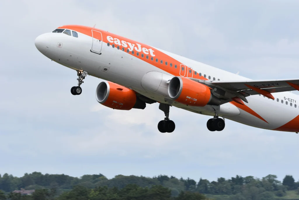 EasyJet passenger jet lifting off with gear down, orange and white livery, engines visible against a cloudy sky.