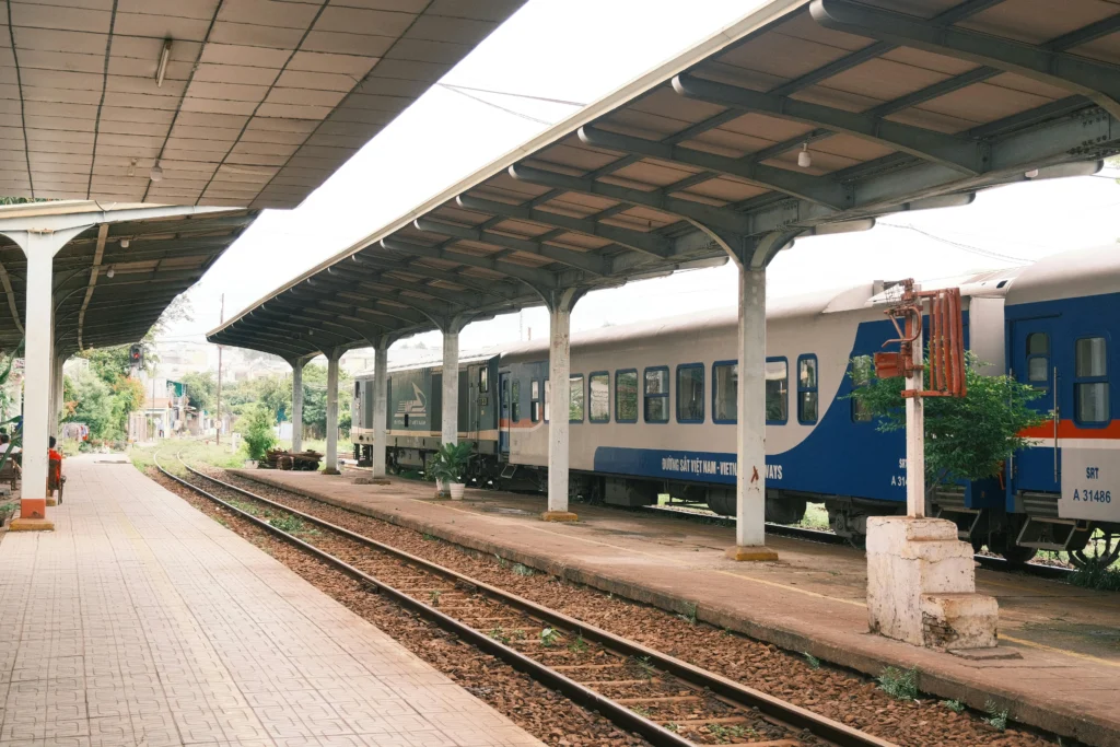 Passenger train at a sheltered platform, blue and white cars beside the tracks with a running line in the foreground.