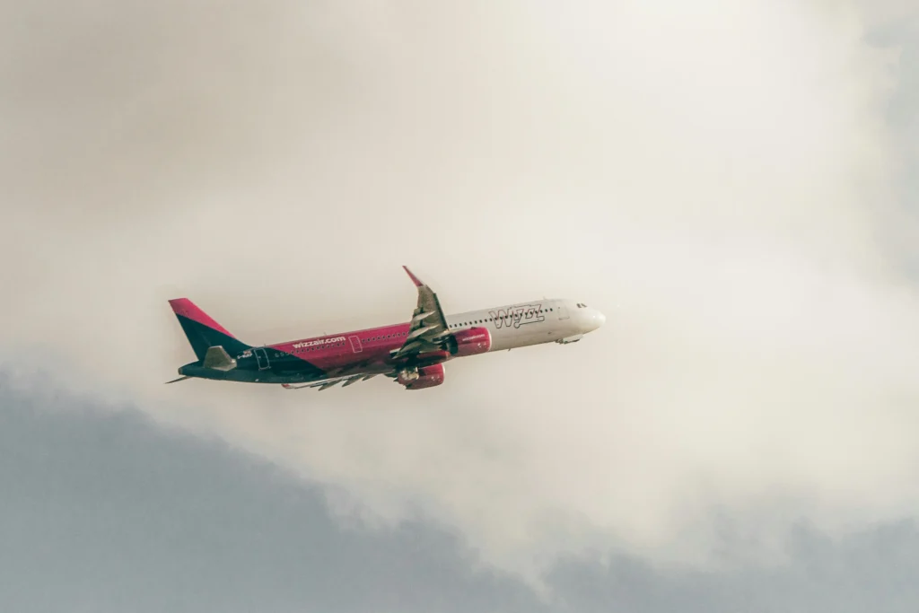 Wizz Air passenger jet flying through a cloudy sky with a pink fuselage and green tail.