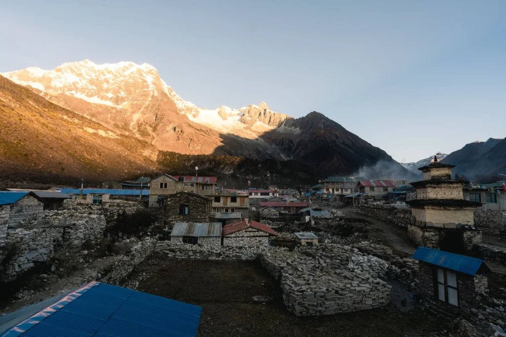 Stone houses with blue roofs in a mountain village beneath snow-capped peaks beneath a clear sky.