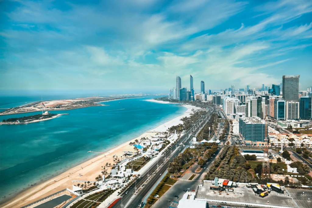 Aerial view of a coastal city with a sandy beach, turquoise water, and a high-rise skyline along the waterfront.