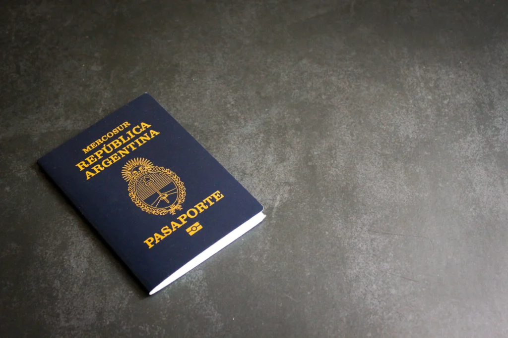 Blue passport partially visible in the bottom-left corner on a gray textured surface, showing gold lettering and emblem.