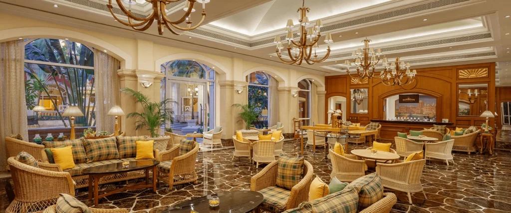 Luxurious hotel lobby with wicker sofas, plaid cushions, and yellow accents on a marble-tiled floor.