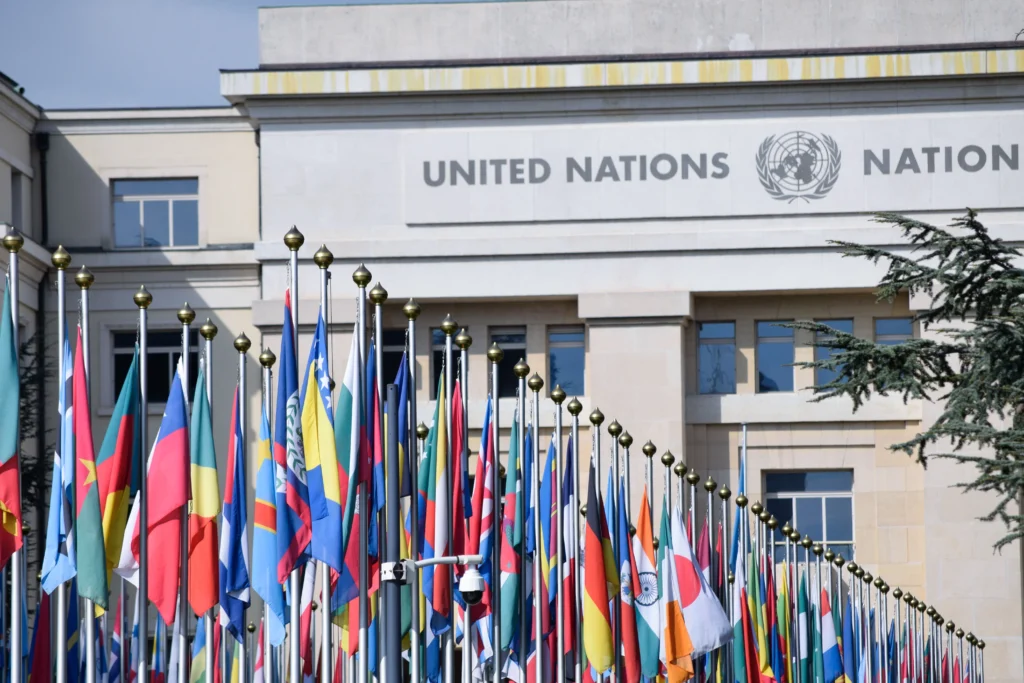Front of a United Nations building with dozens of colorful national flags on flagpoles.