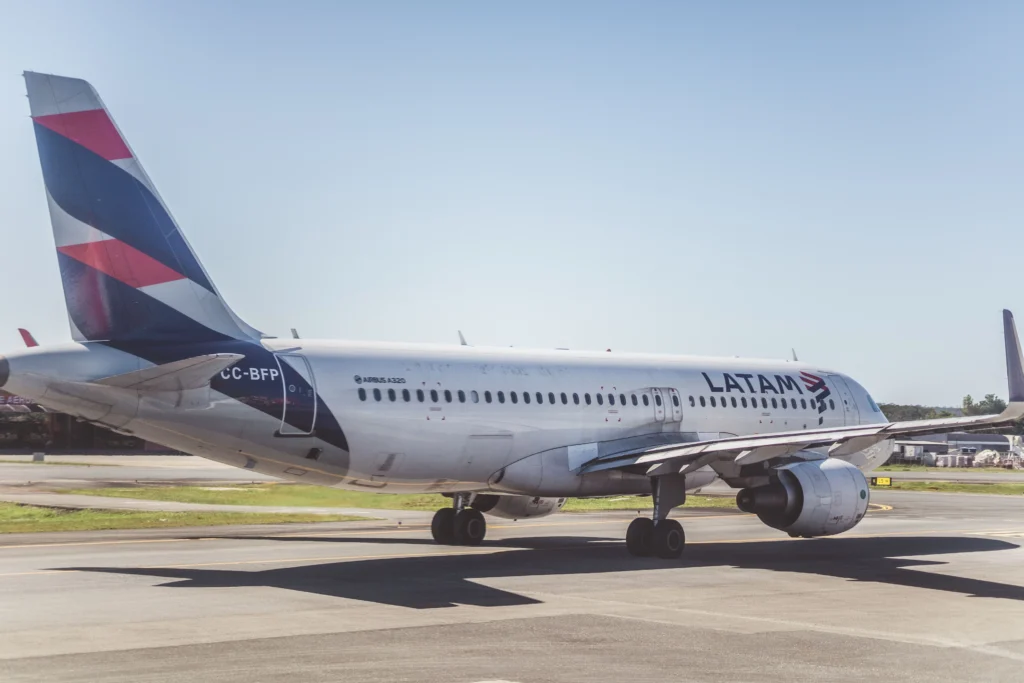 Side-view of a LATAM Airbus A320 on the tarmac, tail painted with red, white, and blue stripes showing on the left.