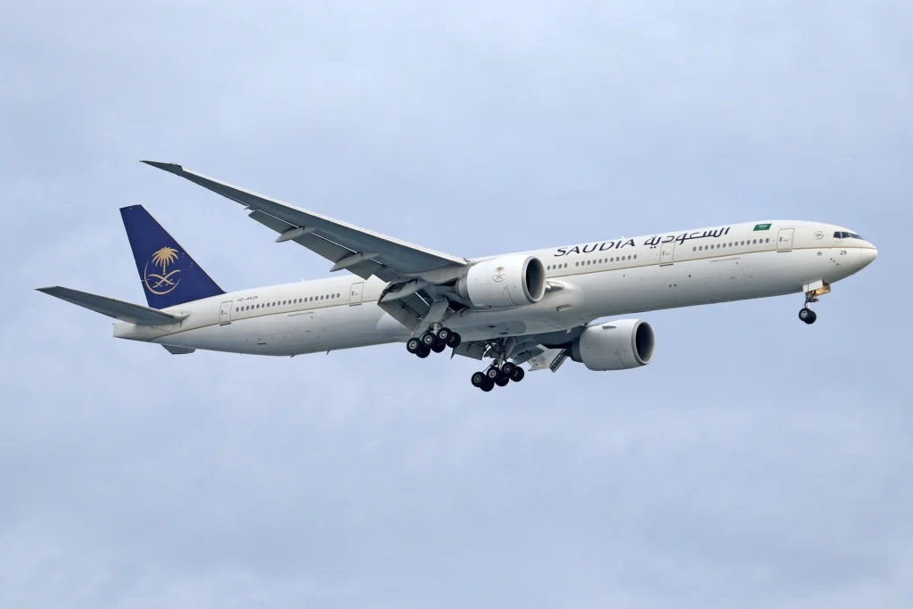 Saudi Arabian Airlines wide-body aircraft in flight, left-side view with landing gear down and blue tail logo with a palm tree