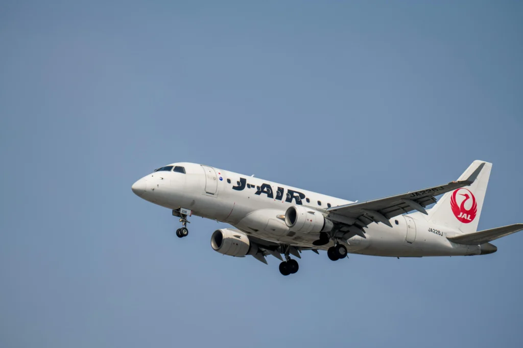 White Japan Airlines aircraft in flight with landing gear down against a clear blue sky, nose slightly up in approach position
