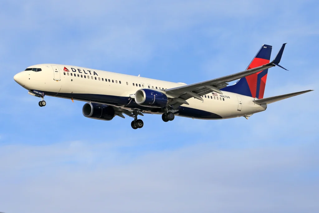 Delta Air Lines passenger jet flying in clear blue sky with landing gear extended.