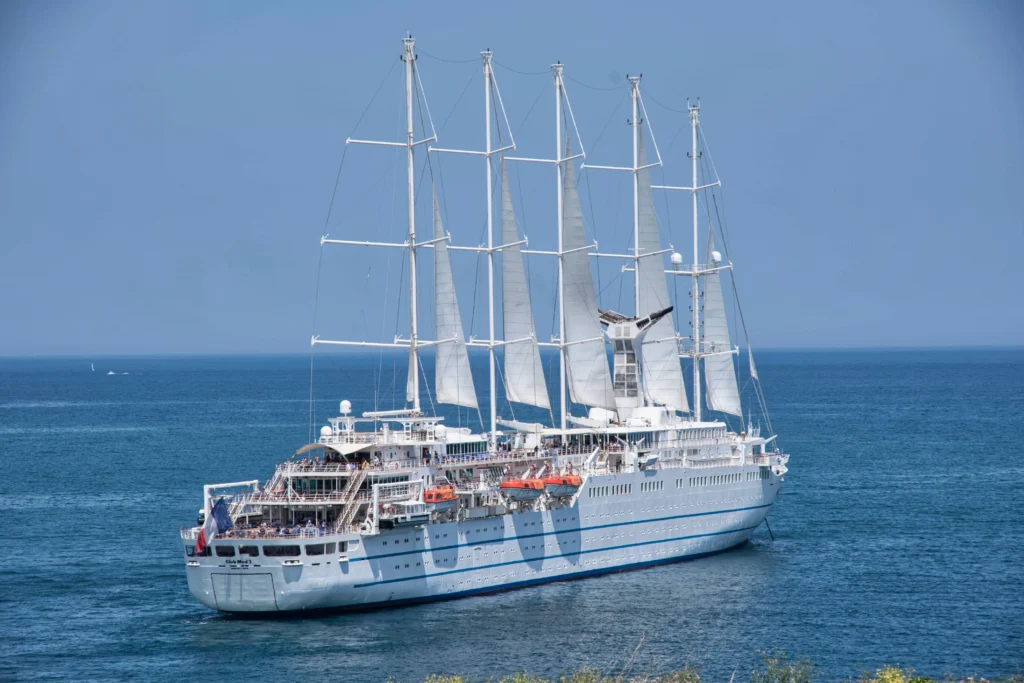 Large white cruise ship with tall masts and rigging anchored on calm blue sea under a clear sky.