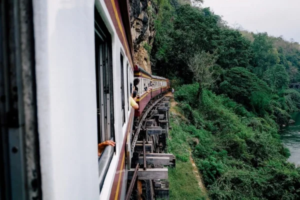 Passenger train runs along a cliffside track with riders leaning out of windows to view the scenery below.