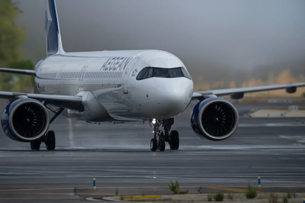 Front view of a white commercial airliner on the runway, Aegean branding visible on the fuselage, engines at the wings.