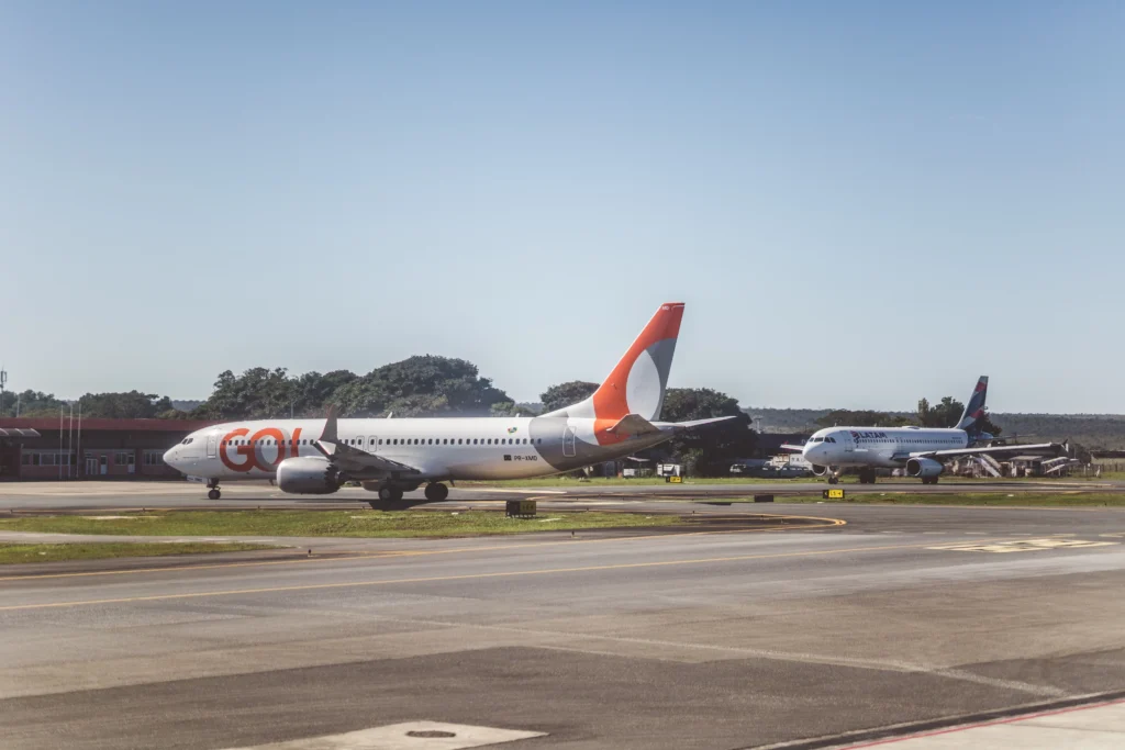 GOL Airlines jet taxiing on the tarmac with a LATAM plane in the background under a clear blue sky.