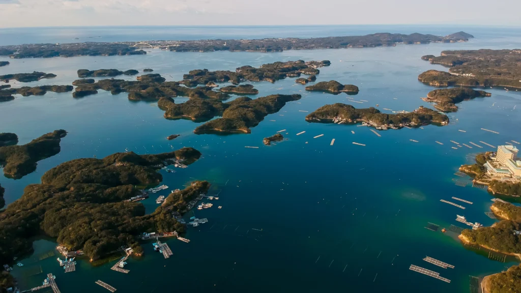Aerial view of numerous small, forested islands in a calm blue sea with scattered docks and boats.