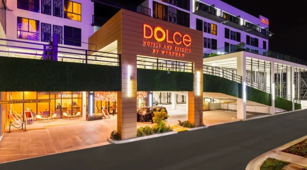 Night exterior of Dolce Hotels by Wyndham with a lit red sign, glass storefronts, and outdoor seating area.