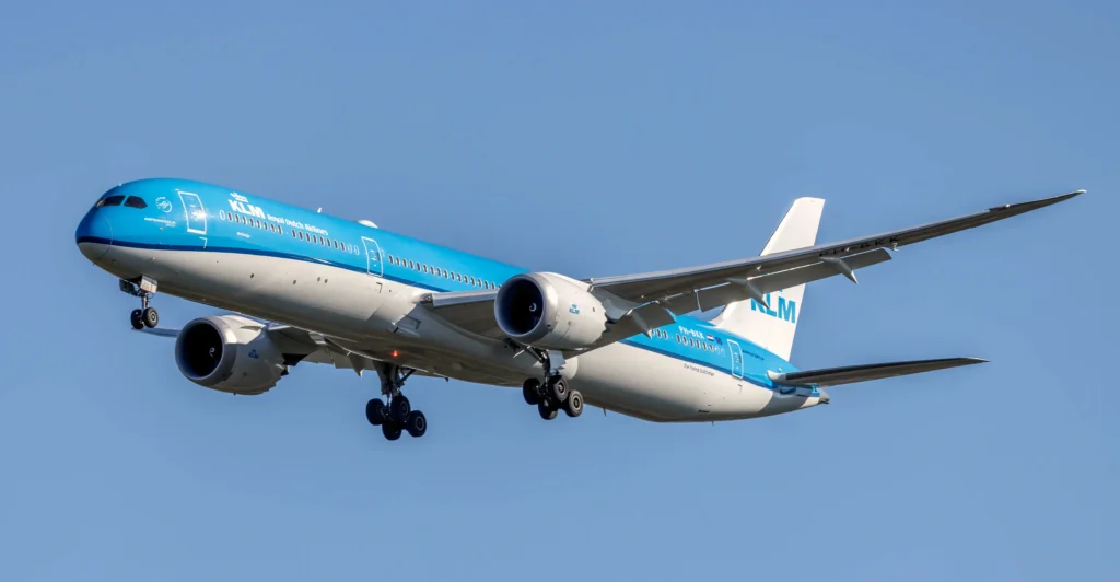 KLM Boeing 787 Dreamliner in blue livery, landing with gear down against a clear blue sky.