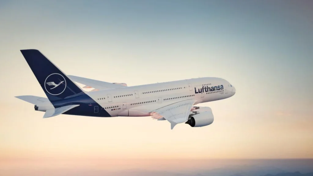Lufthansa airplane in flight against a pale sunset sky, blue tail with logo visible
