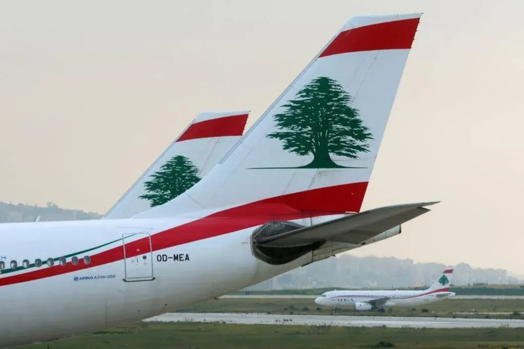 Two Middle East Airlines jets on the tarmac, showing the red-and-white tails with a green cedar logo and a distant arriving plane in the background.
